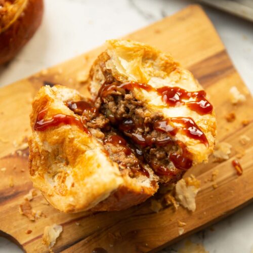 close up shot of beef bread roll pie in half on chopping board with brown sauce