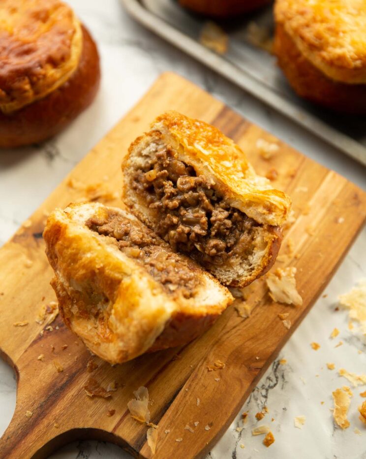 bread roll beef mince pie on chopping board sliced in half to show filling
