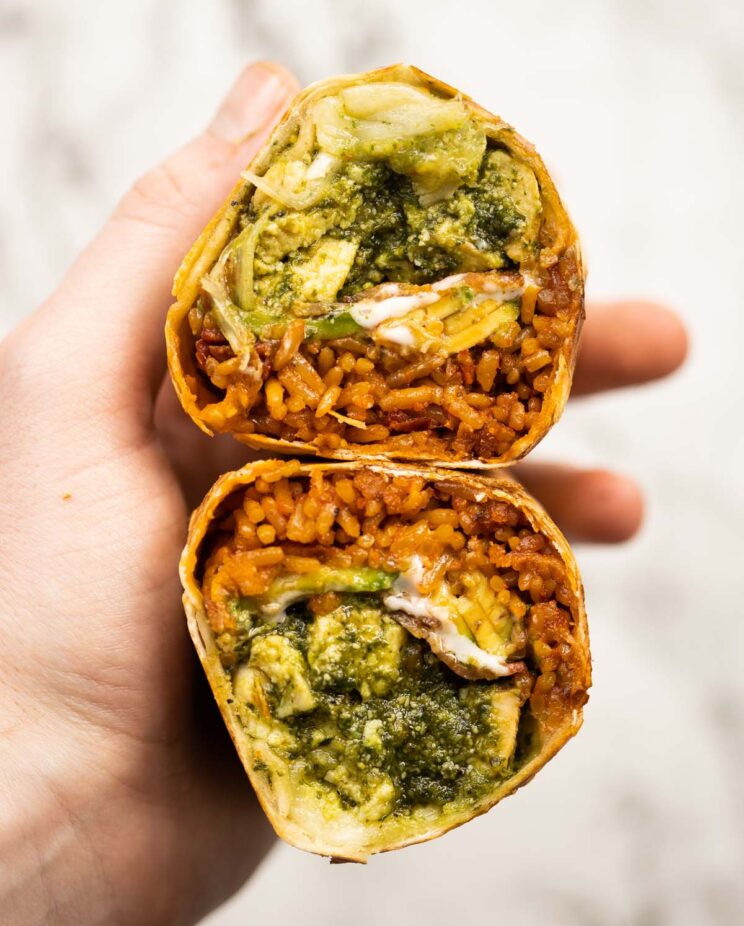 close up overhead shot of hand holding chicken pesto burrito sliced open showing filling