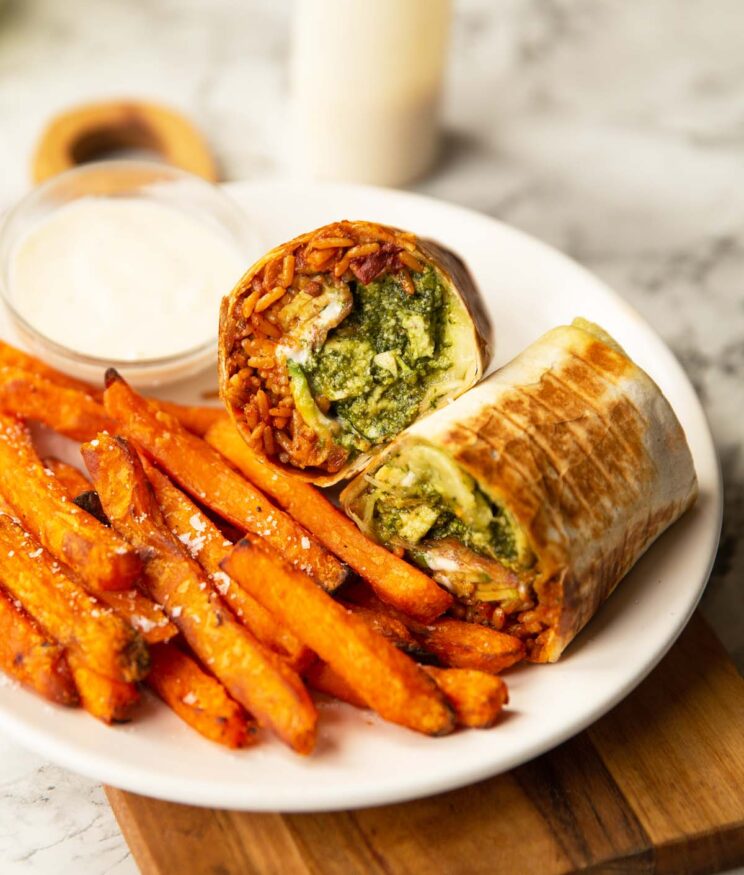 chicken pesto burrito wrap on large white plate with sweet potato fries and pot of caesar dressing