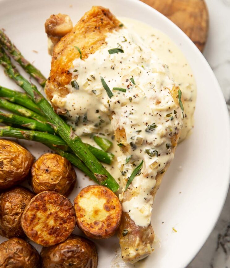close up overhead shot of creamy mustard tarragon chicken on small white plate with potatoes and asparagus